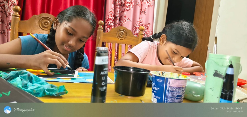 Two girls painting at a wooden table during Children's Day